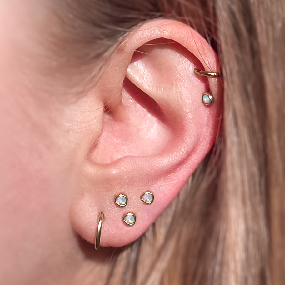 Een oor met 4 galaxy opal studs in 14-karaats geelgoud